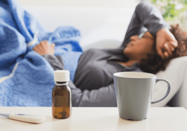 woman feeling unwell sick lying down with medication and drink on table